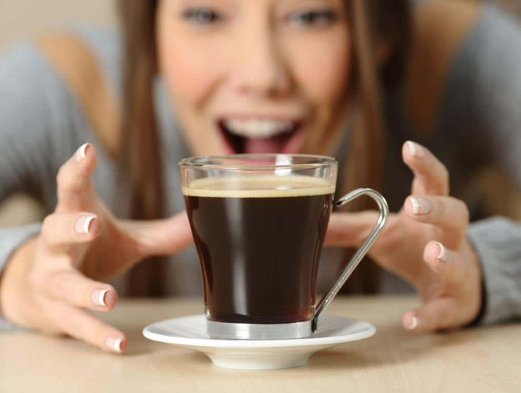 Front view close up of an amazed woman looking at a coffee cup with crave