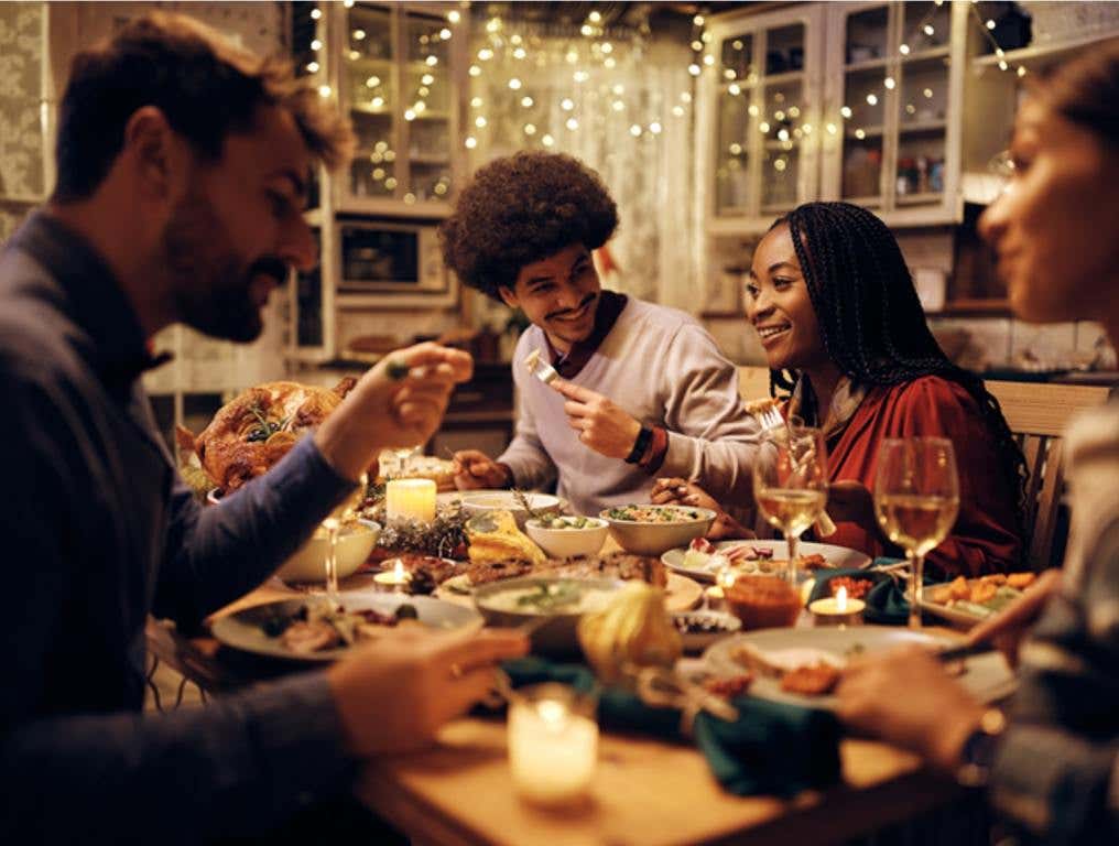 Group of happy friends eating at dining table while celebrating Thanksgiving together, Friendsgiving concept