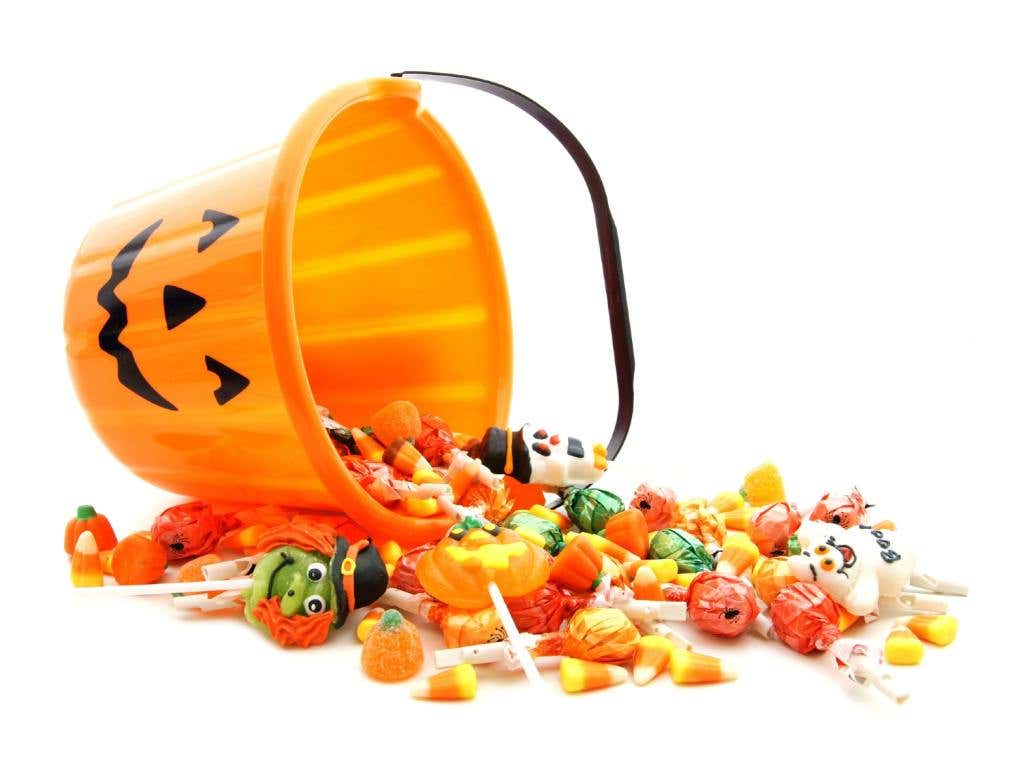 Halloween jack-o-lantern pail with spilling candy over white, trick or treat handouts, Halloween hand out concept.