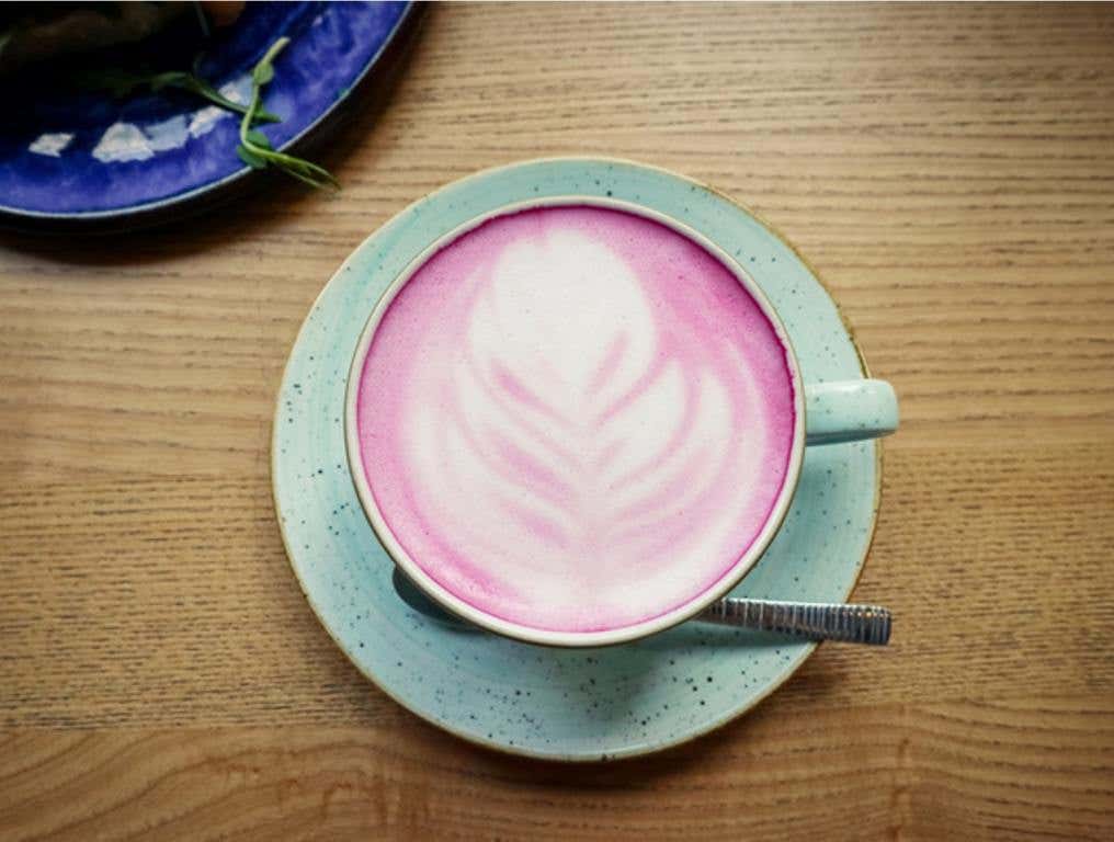 Cup of pink cappuccino in blue cup on wooden table in a cafe closeup, top view, mean girls pink creamer concept.