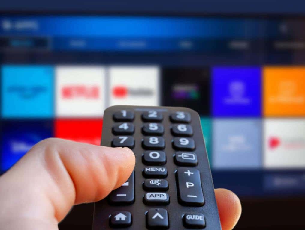 A man is holding a remote control of a smart TV in his hand. In the background you can see the television screen with streaming entertainment apps for video on demand, streaming Netflix concept