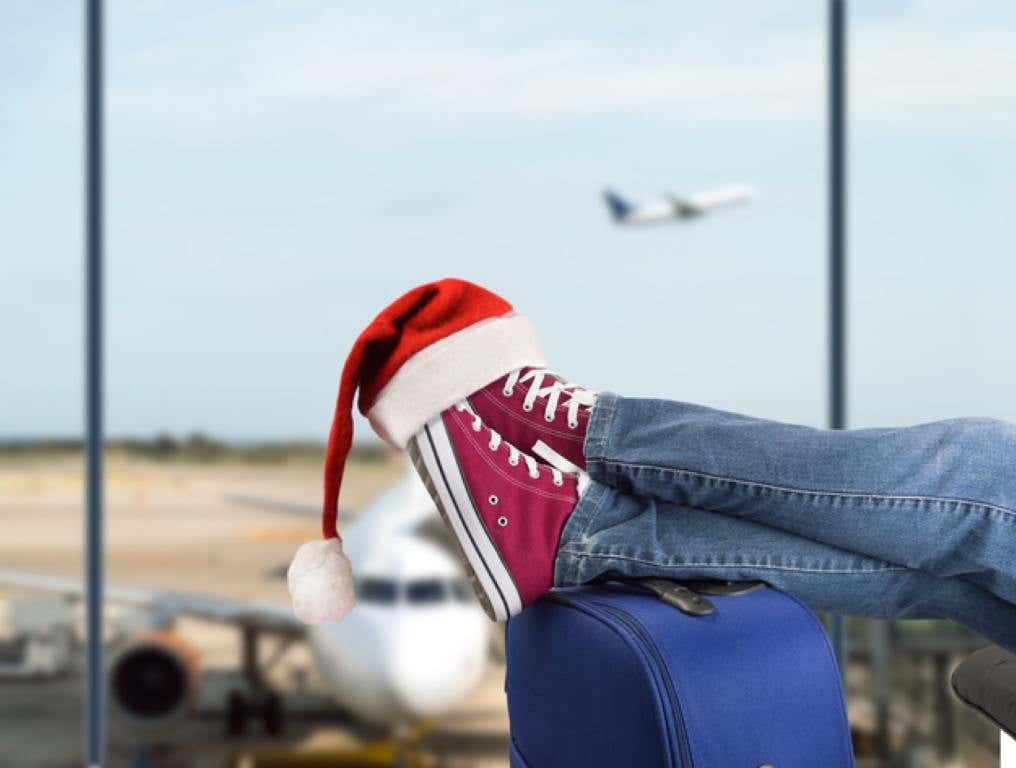 young boy with his legs over the suitcase waiting at the airport with santa hat on the feet, holiday travel concept