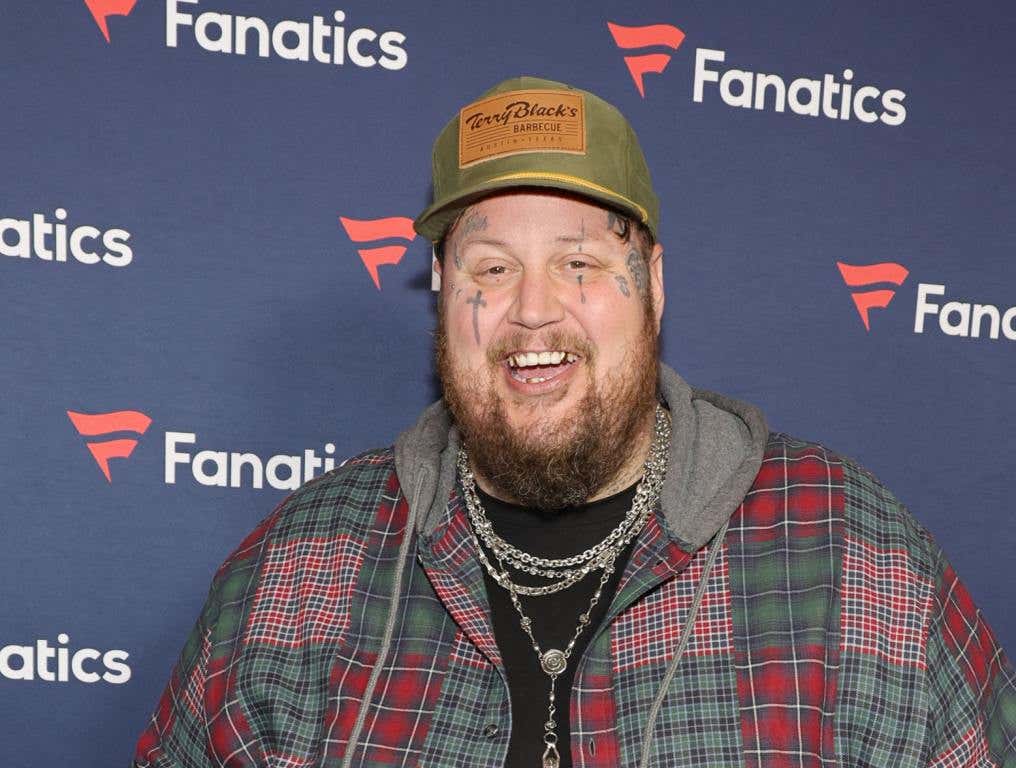 Jelly Roll's Father - Jelly Roll wearing a plaid shirt, tan hat, and smiling on a red carpet.