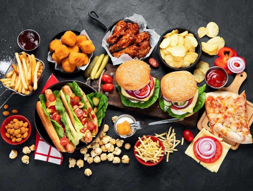 Some of Nevada's favorite fast food restaurants serve meals similar to the ones displayed on a black tabletop in this overhead view photo. Fast food items include french fries, tater tots, chicken wings, potato chips, pizza, popcorn, hamburgers, and hot dogs. There are also some condiments in the photo including ketchup, barbecue sauce, pickles, and ranch dressing.