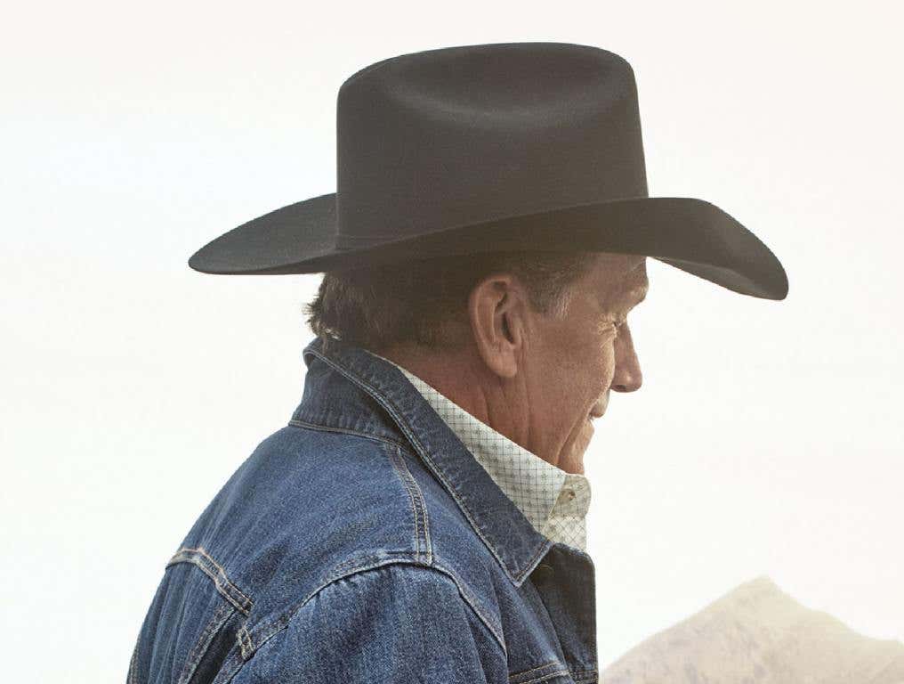 George Strait, wearing a cowyboy hat and a denim jackte, posing from the side.