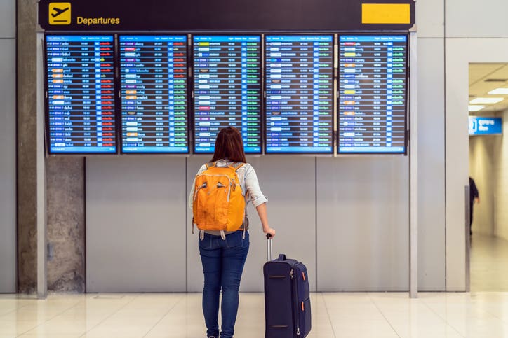 Back side of traveler with luggage standing over the flight board for check-in at the flight information screen in modern an airport, travel and transportation with technology concept.