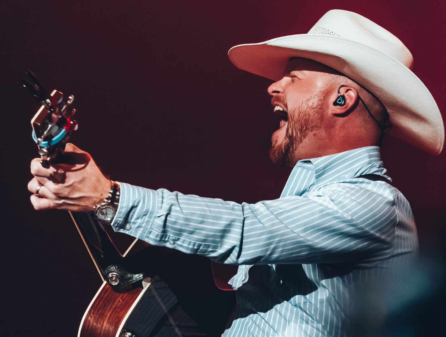 Cody Johnson is performing live playing guitar in a cowboy hat and a blue shirt with white pinstripes.