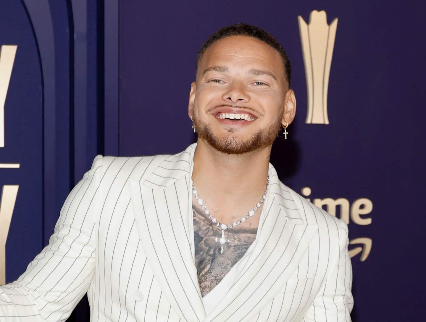 Kane Brown is wearing a white striped blazer on a red carpet.