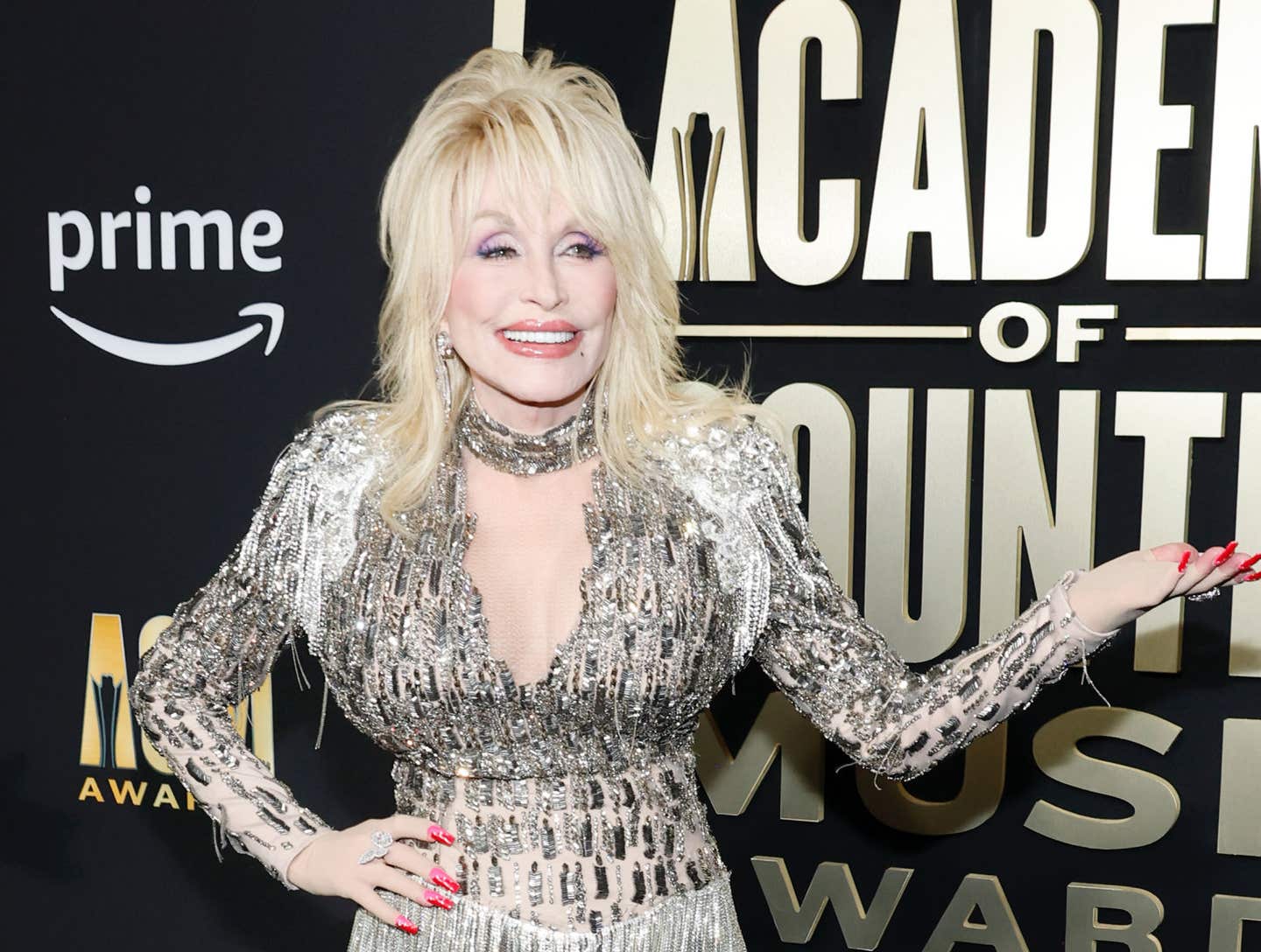 Dolly Parton posing on a red carpet in a black and gold dress.