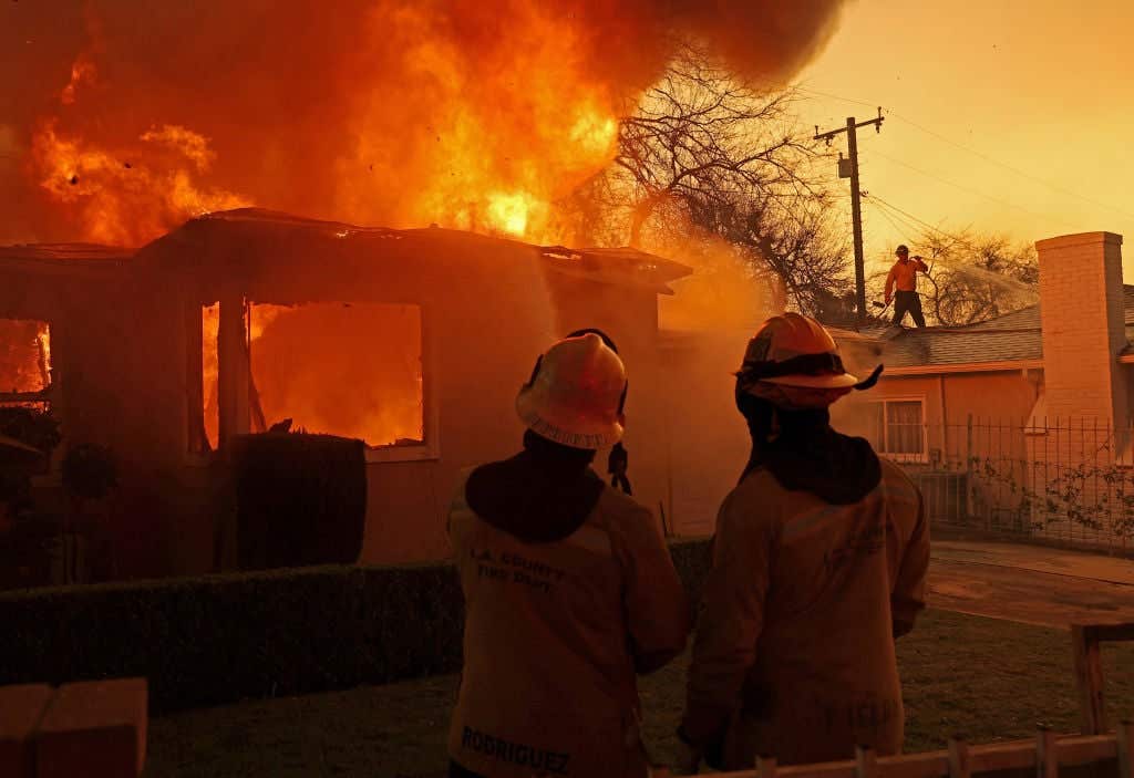 Los Angeles County firefighters spray water on a burning home as the Eaton Fire moves through the area on January 08, 2025 in Altadena, California.