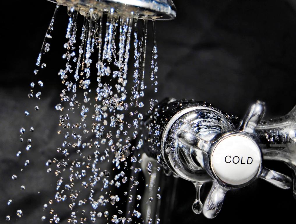 Chrome bath tap and water flowing from shower head. Cold showers have shown to have some of the same benefits as an ice bath.