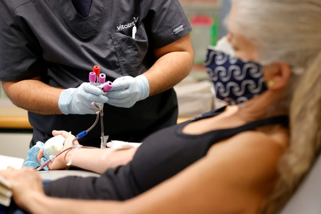 A phlebotomist collect vials of blood from an intravenous line from a patient who is donating blood at Vitalant blood donation center.